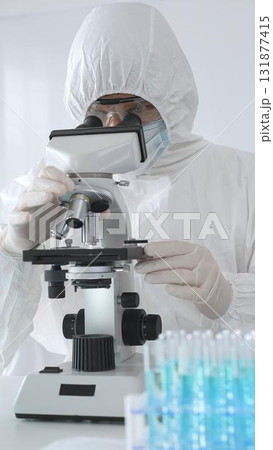 Medical scientist wearing protective suit using microscope while analyzing samples, conducting research in laboratory environment. Close up of test tubes with blue liquid 131877415