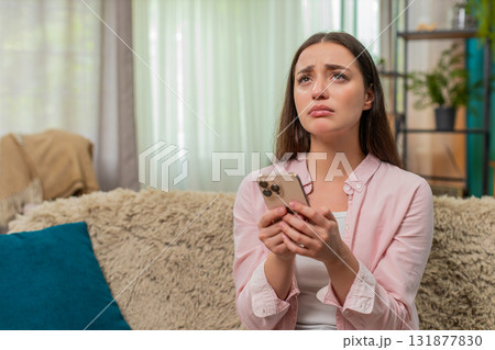 Young woman frowning at smartphone after contest loss shows sad reaction and very strong frustration Young woman frowning at smartphone after contest loss shows sad reaction and very strong frustration 131877830