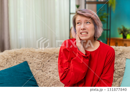 Young woman holding cheek experiencing toothache pain, painful uncomfortable facial expression home 131877840