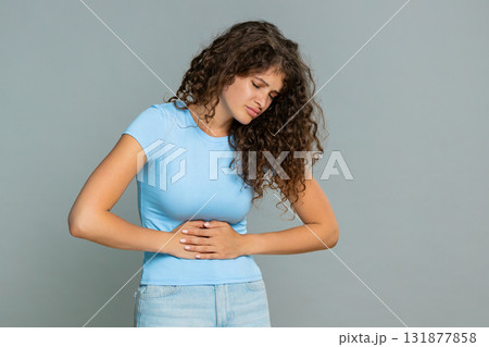Woman suffering sharp stomach pain holding abdomen bending forward discomfort unhealthy reaction Woman suffering sharp stomach pain holding abdomen bending forward discomfort unhealthy reaction 131877858