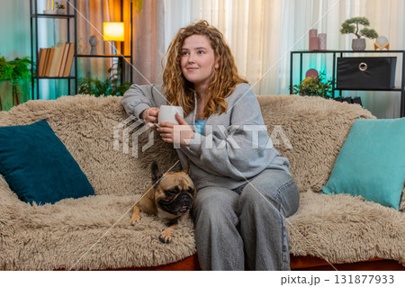 Young woman drinking coffee with pug dog near on home sofa, peaceful morning atmosphere and joy 131877933