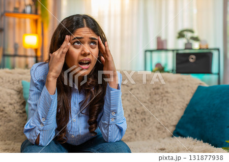 Indian woman touching head with tension and pain from headache at home, exhausted and uncomfortable Indian woman touching head with tension and pain from headache at home, exhausted and uncomfortable 131877938