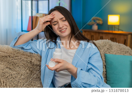 Woman suffering severe headache sitting holding head exhausted searching taking pain relief pills 131878013
