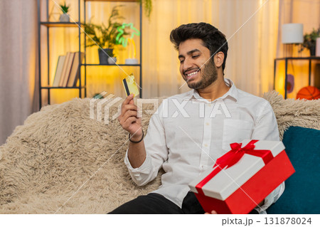 Indian worried man holding credit card, making online purchase, receiving gift, reacting emotionally 131878024
