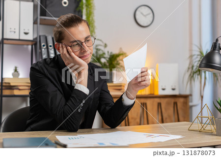 Serious businessman sitting at home office desk with letter reading bad news upset and disappointed 131878073