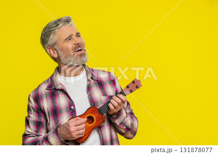 Happy mature man playing on toy guitar ukulele shaking head and dancing enjoying rhythm of music Happy mature man playing on toy guitar ukulele shaking head and dancing enjoying rhythm of music 131878077