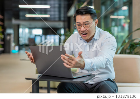 Sad businessman using laptop loses becoming shocked sudden lottery results in modern hotel lobby Sad businessman using laptop loses becoming shocked sudden lottery results in modern hotel lobby 131878130