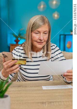 Mature woman using credit card and smartphone to transfer money, pay bills, sitting on table at home Mature woman using credit card and smartphone to transfer money, pay bills, sitting on table at home 131878131