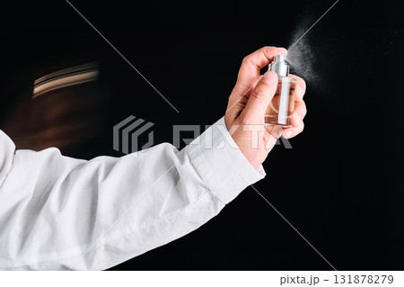 A hand in a white shirt sprays perfume or air freshener. Black background. A hand in a white shirt sprays perfume or air freshener. Black background. 131878279
