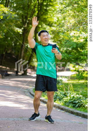 Athletic fitness Asian sport runner man walking, wearing headphones listening music from smartphone Athletic fitness Asian sport runner man walking, wearing headphones listening music from smartphone 131878349