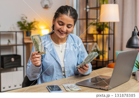 Happy rich Indian freelancer counting money cash using smartphone calculator app at home office desk Happy rich Indian freelancer counting money cash using smartphone calculator app at home office desk 131878385