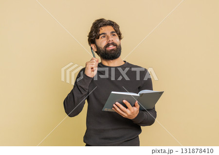 Thoughtful businessman making notes, writing down thoughts with pen into diary on beige background 131878410