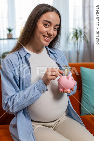 Pregnant woman inserting banknote money cash dollar in piggybank saving for baby's future needs 131878416