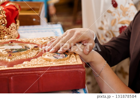 Orthodox Wedding Ceremony: Hands Holding a Holy Book, Red and Gold Icons, Traditional Ritual, Faith, Love, and Marriage in Church Setting Orthodox Wedding Ceremony: Hands Holding a Holy Book, Red and Gold Icons, Traditional Ritual, Faith, Love, and Marriage in Church Setting 131878584
