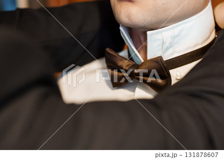 Stylish Man Adjusting Brown Bow Tie with Crisp White Shirt, Formal Black Tuxedo, Close-Up, Elegant, Sophisticated, Fashion, Groom, Wedding, Texture. 131878607