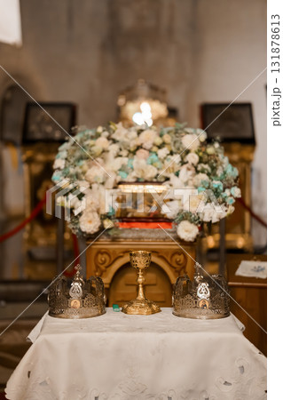 Orthodox Wedding Ceremony Detail: Floral Altar Arrangement with Crowns, Golden Chalice, and Religious Icons in Church Interior Orthodox Wedding Ceremony Detail: Floral Altar Arrangement with Crowns, Golden Chalice, and Religious Icons in Church Interior 131878613