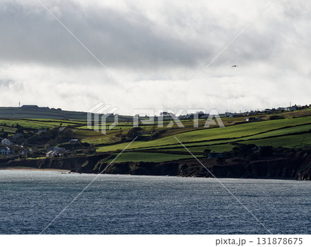 Scenic view of green hills and ocean waters at Dunmore Bay Beach in Ireland under cloudy skies. Scenic view of green hills and ocean waters at Dunmore Bay Beach in Ireland under cloudy skies. 131878675