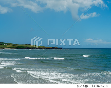 This is a view of the ocean on a sunny day in West Cork. Waves are moving toward the sandy beach. Grass and a house are visible along the coastline in Ireland. This is a view of the ocean on a sunny day in West Cork. Waves are moving toward the sandy beach. Grass and a house are visible along the coastline in Ireland. 131878700
