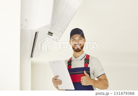 Happy technician approving air conditioner installation, checking split system indoor unit installed 131879366