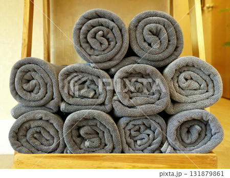 Rolls of gray towels are stacked on a wooden shelf. 131879861