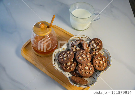 Side angle view of a tray holding cookies, honey jar, and a milk mug on table. Close-up of holiday snack arrangement, upper body or people not visible. Side angle view of a tray holding cookies, honey jar, and a milk mug on table. Close-up of holiday snack arrangement, upper body or people not visible. 131879914