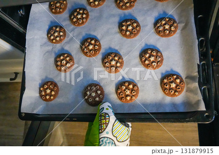 Top view photo of hand wearing oven mitt taking out hot tray with baked cookies from oven. Holiday cooking concept, homemade pastry, Christmas dessert preparation. Top view photo of hand wearing oven mitt taking out hot tray with baked cookies from oven. Holiday cooking concept, homemade pastry, Christmas dessert preparation. 131879915