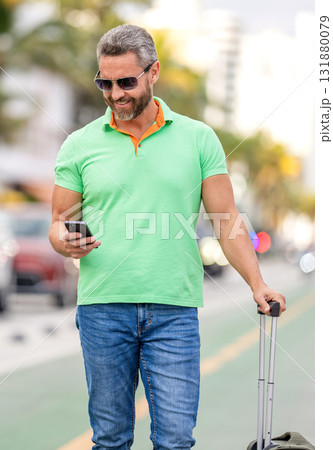 Traveler using phone. Tourist booking vacation trip. Traveler suitcase for summer trip. Man booking summer trip. Hispanic tourist traveler book online outdoor. Tourist with travel bag 131880079