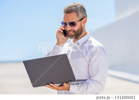 Successful businessman freelancing online. Hispanic business man working online. Remote working. Phone call communication. Businessman busy working on laptop outdoor. Man has business phone call Successful businessman freelancing online. Hispanic business man working online. Remote working. Phone call communication. Businessman busy working on laptop outdoor. Man has business phone call 131880081