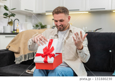 Young man lifts lid of gift box finds desired item freezes in surprise smiles with pure joy moment 131880230