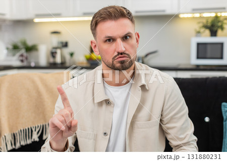 Young man waves finger no no at camera shows firm refusal and disagree sign with serious calm face 131880231