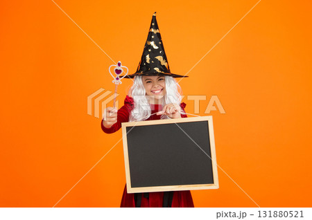 Girl in witch costume hold magic wand. Happy Halloween advertisement. Girl witch in Halloween costume isolated on orange. Halloween party advertisement. Hallows witch girl. Halloween sale Girl in witch costume hold magic wand. Happy Halloween advertisement. Girl witch in Halloween costume isolated on orange. Halloween party advertisement. Hallows witch girl. Halloween sale 131880521