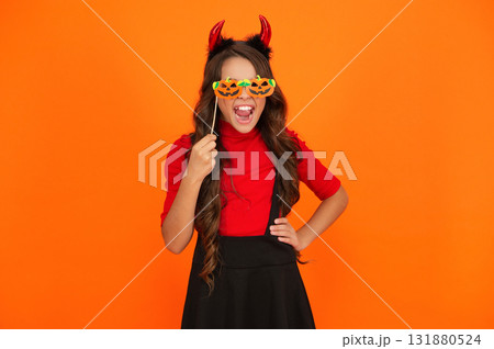 Girl devil in Halloween costume isolated on orange. Trick or treat. All Hallows costume party celebration. All Hallows devil. Imp horns. Girl in Halloween imp costume. Happy Halloween. Sharp horns 131880524