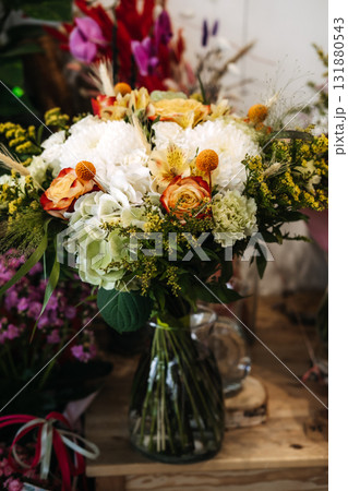 Autumn floral arrangement displayed in a clear glass vase on wooden surface. Seasonal bouquet design, cozy flower shop vibes, rustic natural decor, local florist craftsmanship 131880543