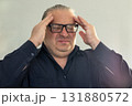 Man with glasses holds temples, showing stress and headache in a studio portrait 131880572