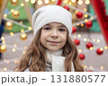 Young girl in white hat and scarf smiling among Christmas lights and baubles 131880577