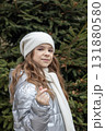 Young girl in white knit hat and scarf stands outdoors in a winter forest portrait 131880580