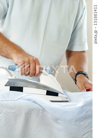 Man ironing a shirt on an ironing board in a well-lit room 131881411