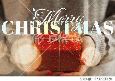 Person holding a red Christmas gift wrapped with twine in a cozy indoor setting 131881576
