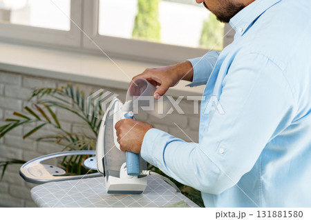 Man ironing clothes in a bright room with a domestic atmosphere during daytime Man ironing clothes in a bright room with a domestic atmosphere during daytime 131881580