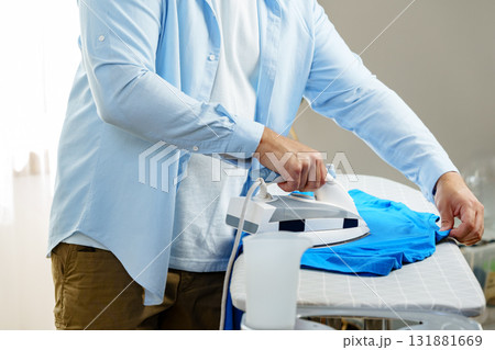 Ironing a blue shirt while preparing laundry in a bright room 131881669