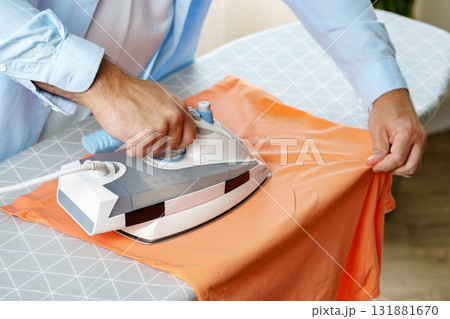 Ironing a bright orange shirt on an ironing board in a well-lit room during the day 131881670