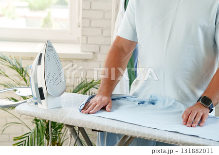 Man ironing a shirt at home on a sunny afternoon in a cozy living room 131882011