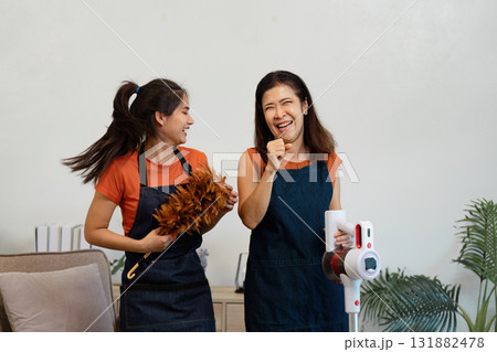 Mother and daughter joyfully cleaning together in their living room 131882478