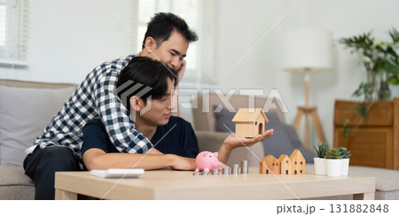 LGBT Couples Building Dreams. A couple lovingly discusses their future plans while holding a model house and piggy bank. 131882848