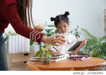 Learning and Nurturing. A mother attends to her daughter while she works on her school tasks. 131882881