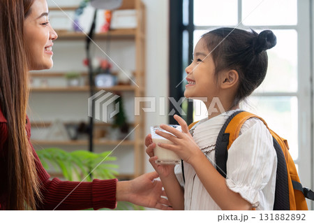 Breakfast and School Readiness. A young girl enjoys a nutritious drink while preparing for her school day with her mother. 131882892