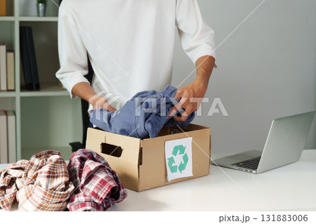 Clothing Recycling and Sustainability. A person sorting through clothes, preparing to donate them for recycling in an eco-conscious effort. Clothing Recycling and Sustainability. A person sorting through clothes, preparing to donate them for recycling in an eco-conscious effort. 131883006