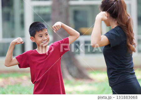Strength Training and Family Fun. A boy flexes his muscles playfully during an exercise session with his mother. Strength Training and Family Fun. A boy flexes his muscles playfully during an exercise session with his mother. 131883068