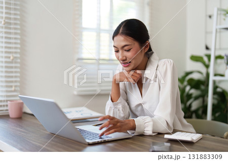 Focused Work and Technology. A young professional engaged in productive online work, navigating her laptop efficiently. Focused Work and Technology. A young professional engaged in productive online work, navigating her laptop efficiently. 131883309