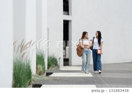 Campus Life and Student Engagement. Two students happily walk through a modern campus environment, embodying the spirit of learning and companionship. 131883438